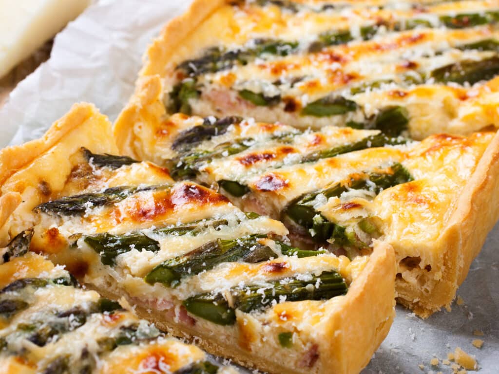 Delicious home made asparagus savory tart with pecorino and bacon on old wooden background.  Selective focus.