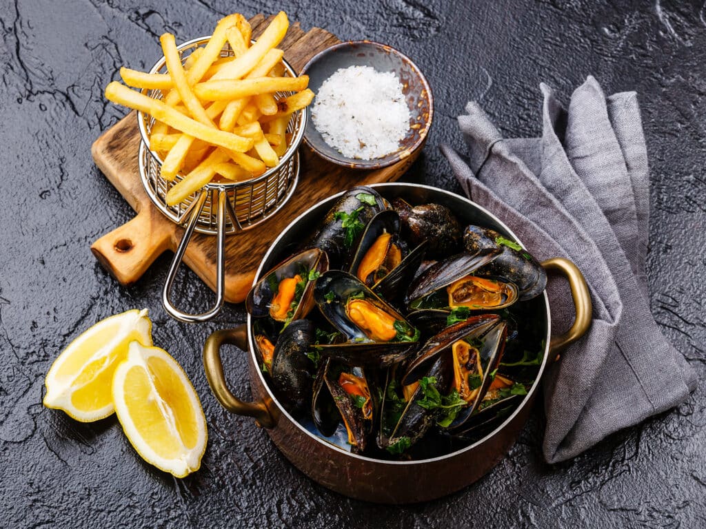 Mussels in copper cooking dish and french fries on black stone background