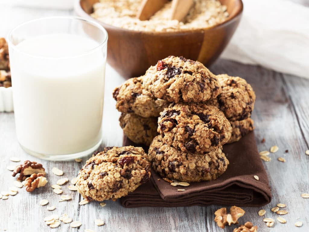 Homemade crunchy oatmeal cookies with dark chocolate and a glass of milk on a white wooden background, selective focus