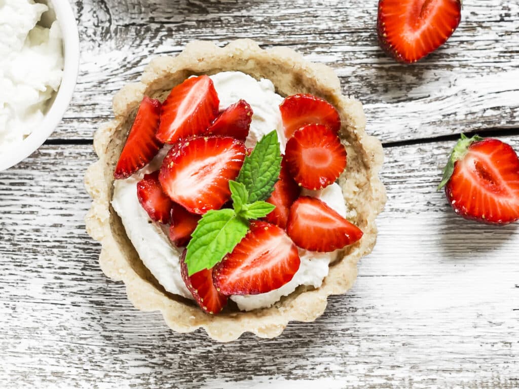 Strawberry tartlet with vanilla cream on a light rustic wooden board. Sweet delicious summer dessert
