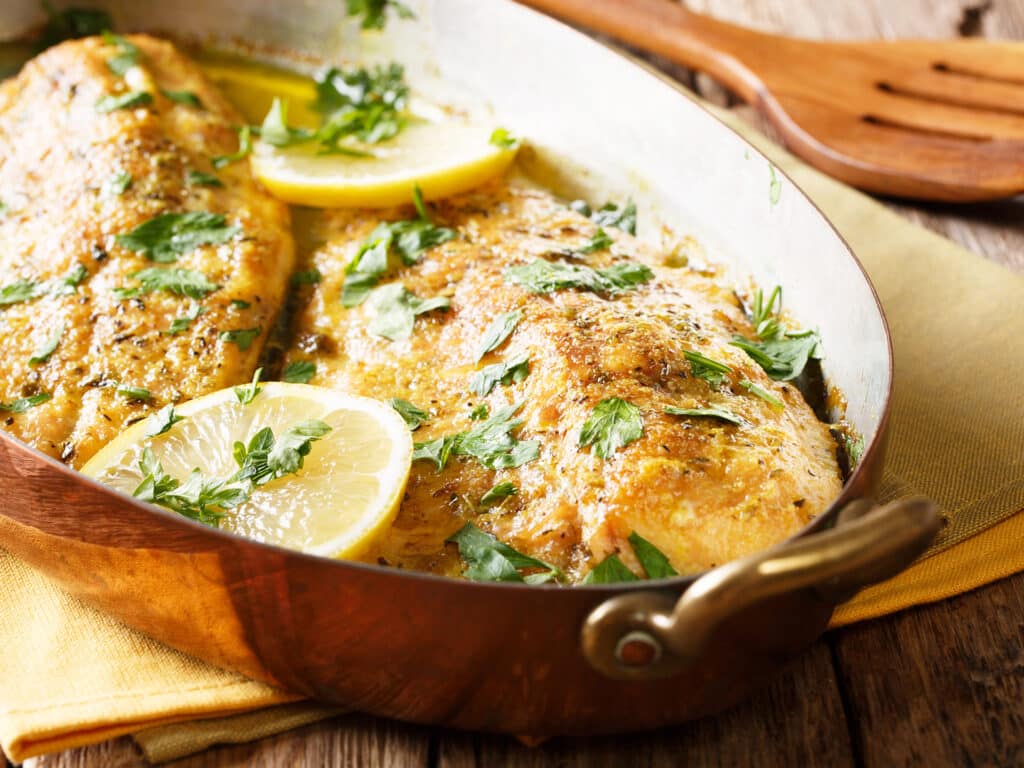 Delicious fish: baked trout fillets with garlic buttery herb sauce, lemon and parsley close-up in a copper frying pan. horizontal
