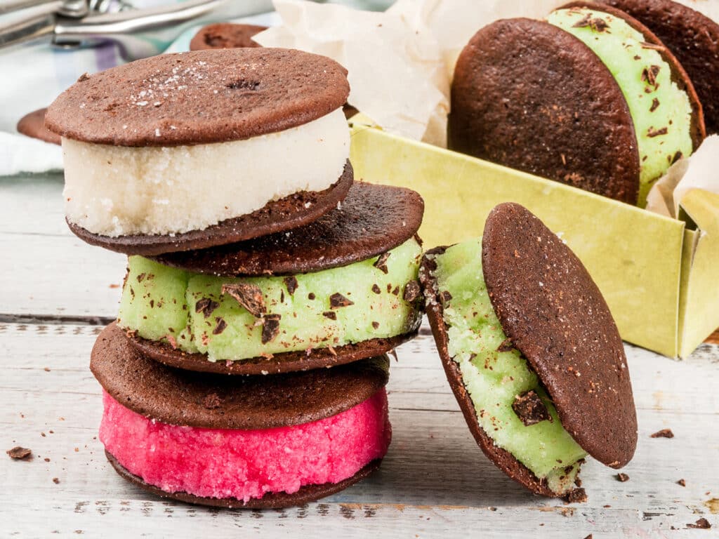 Homemade ice cream sandwich with chocolate cookies whoopie pie. With berry, vanilla and mint ice cream, supplemented with chocolate chips. On a white wooden table. Copy space