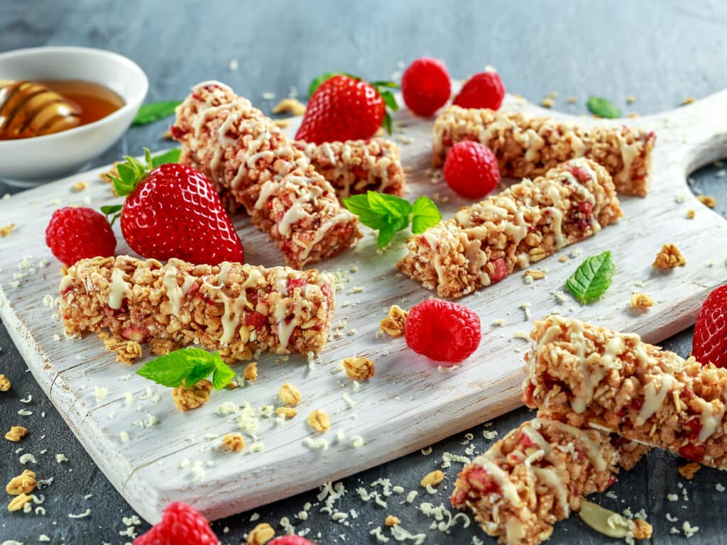 Granola bar with strawberries, raspberry honey and white chocolate on cutting board.