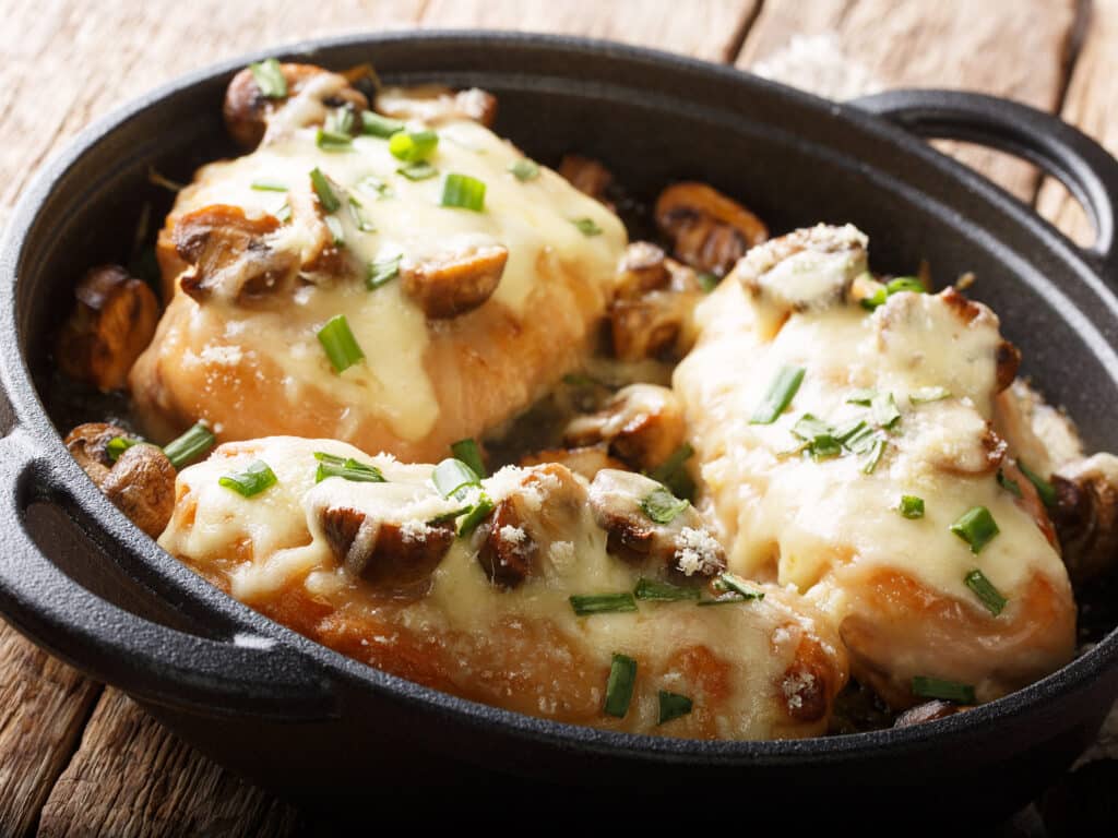 Lombardy Chicken breasts cooked with mushrooms, green onions, mozzarella cheese and parmesan closeup in a pan on the table. horizontal