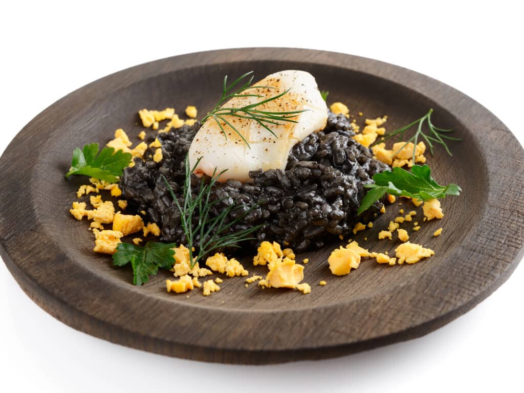 Black squid ink risotto with fried calamari in wooden plate, isolated on white