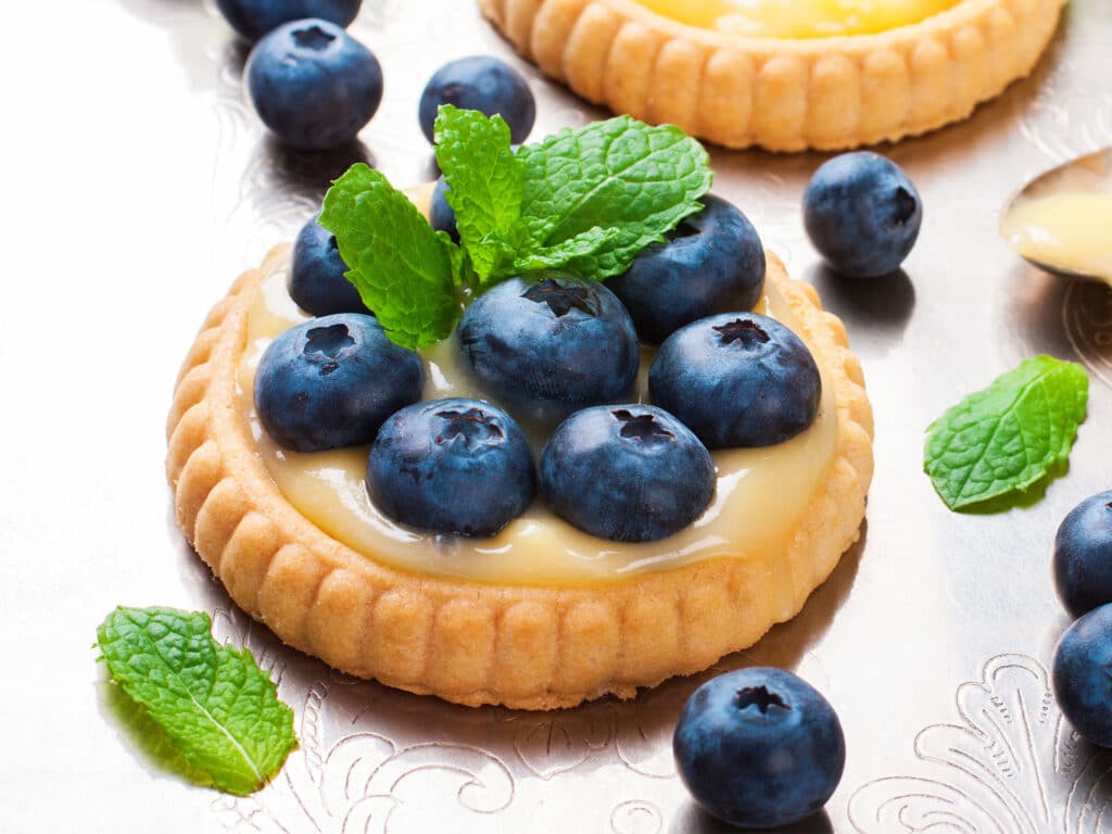Process of making shortbread tartlet filled with lime curd and blueberries on old vintage metal background. Holiday concept. Selective focus.
