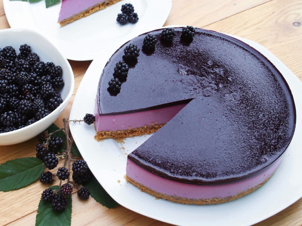 Blackberry cheesecake on a white plate on wooden table. Delicious dessert decorated with fresh fruits