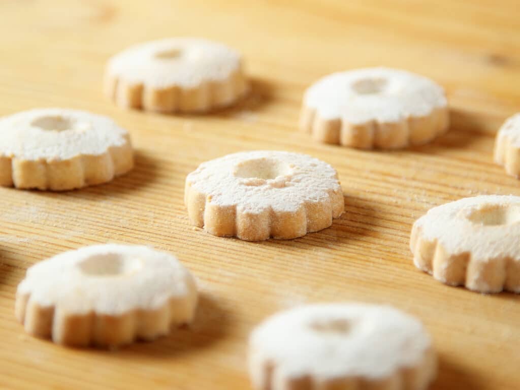 Regular arrangement of italian canestrelli biscuits on a wooden table with powdered sugar on the surface