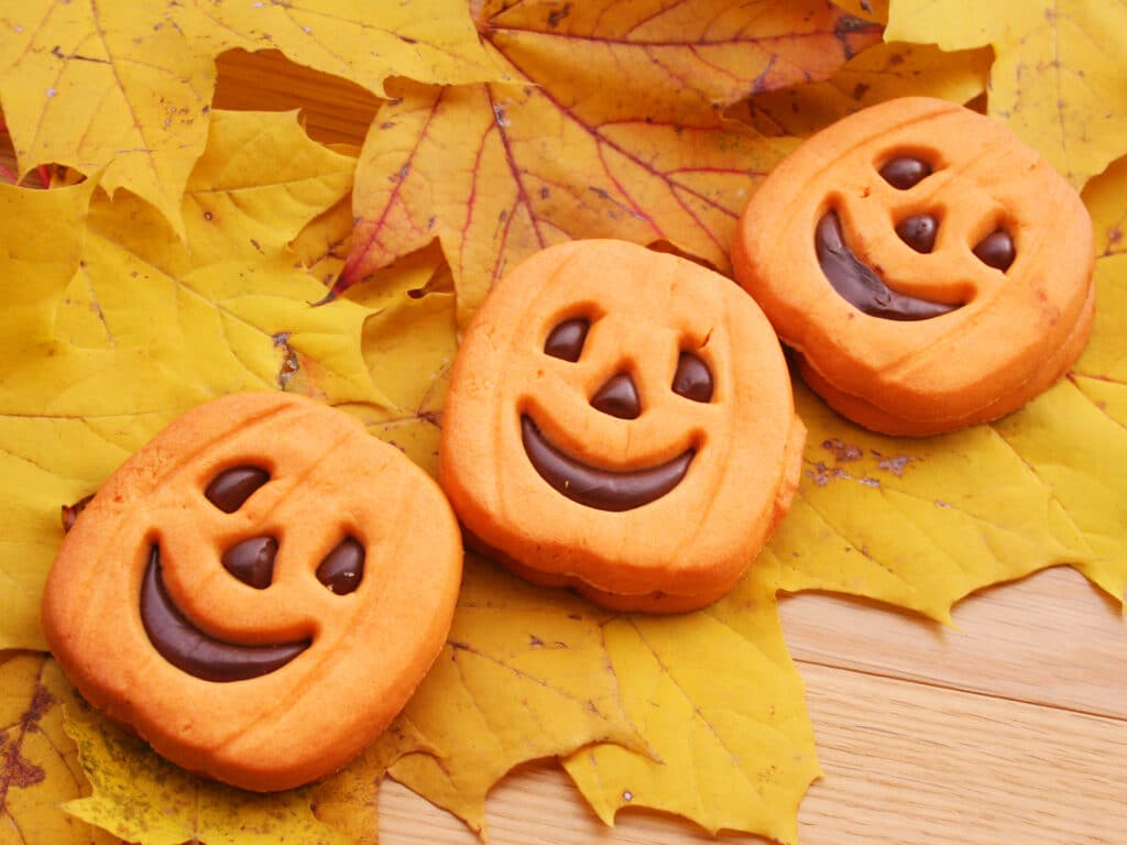 Halloween cookies in shape of a pumpkin filled with choocolate on wooden table with yellow leaves